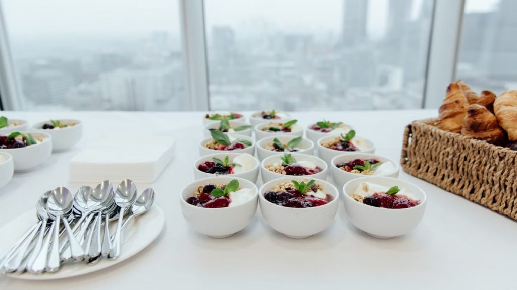 From above of continental breakfast with bowls of yogurt and granola placed in rows near plate with metal shiny clean spoons